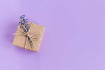 Craft gift box with small lavender bouquet on pastel violet background. Holiday eco-friendly concept.