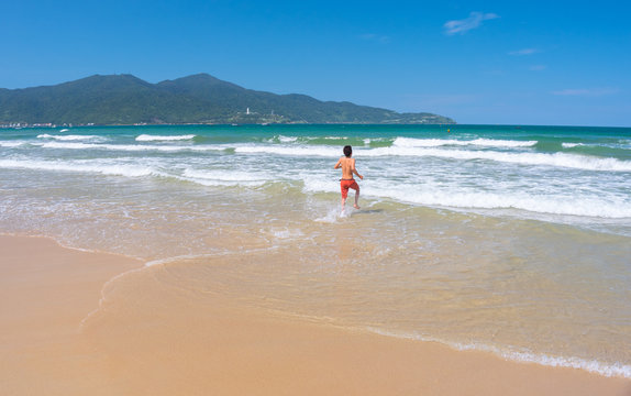 Da Nang Beach: an excited man runs through the surf to the gentle sea waves on My Khe Beach. Son Tra Peninsula and mountain on the horizon. This is the central beach of Danang City, Vietnam, in May.