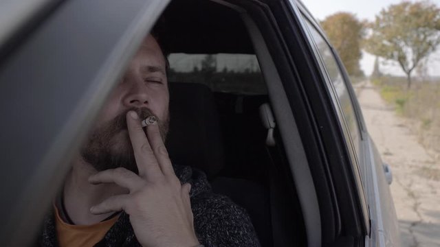 portrait of an attractive bearded man smoking a cigarette while driving a car. smoking guy in a car. 4k. 4k video. slow motion. 23.98 fps