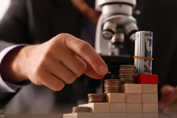 Hand businessman in suit hold quarter in background looking through microscope closeup search business concept