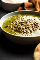 Black Masoor Dal fry or Dhaba Style Sabut Red Lentil dhal tadka in green curry, served in a bowl. selective focus