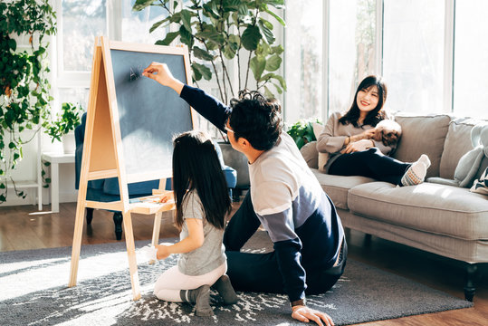 Young father and daughter painting at home, while mother is sitting on sofa with dog