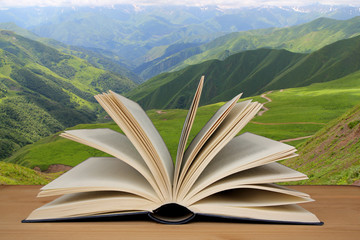 open paper book on a background of natural mountain landscape on a wooden table, literary concept,...
