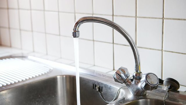 Loopable cinemagraph of running water at stainless steel faucet in kitchen room double sink closeup with two dials and tile backsplash in home 