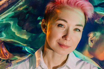 Amazing adult woman with short pink hair by the holographic background looking at camera