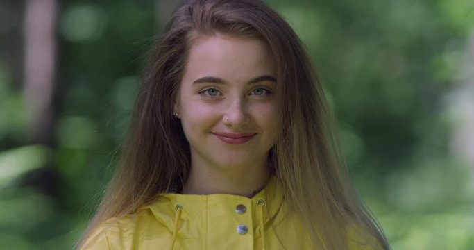 4K Portrait. Young Smiling Woman in a Forest. Student Girl in Yellow Raincoat in British Woods. Pretty Hiker walking in a British Green Trust Park with Natural Sun Light..