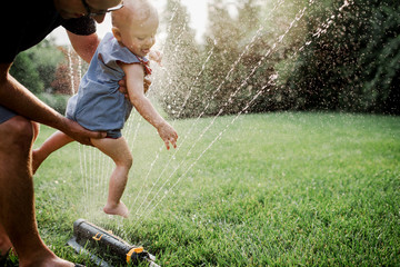 father playing with baby in a sprinkler