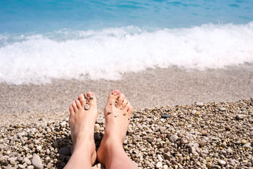 Female feet on a pebble beach on a background of the sea. Vacation at the sea
