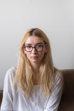 Portrait of a blonde, young female model with glasses at home looking at camera