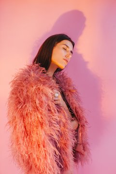 Dreaming woman in feather boa posing by pink background
