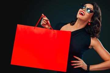 Black Friday sale concept for shop. Happy smiling woman in sunglasses holding big red bag isolated...