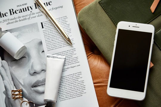 Smartphone, serum and other beauty items over magazine