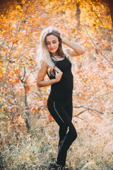 Beautiful attractive girl posing in autumn forest in black pants and t-shirt with beautiful white...