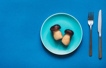 Flat lay - Boletus mushroom on color blue plate with fork and knife on blue background with copy space. Concept of vegetarian diet.