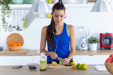 Sporty young woman cutting limes while listening to music in the kitchen at home.
