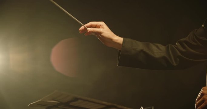 Close up shot of hands of symphony orchesra conductor directing music by waving his baton. Studio shot on black background 4k footage