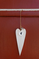 Weißes Herz aus Holz hängt an einer roten Holzwand mit gehäkelter Spitze