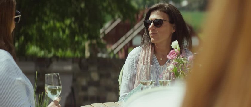 two women are drinking white wine at a restaurant on the patio in the sun and are having a good conversation - Zwei Frauen sitzen in einem Restaurant drau&szlig;en auf der Terasse und trinken Wein