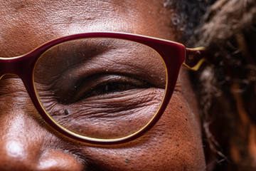 An extreme closeup view on the eye of an elderly African woman wearing reading glasses, jovial and...