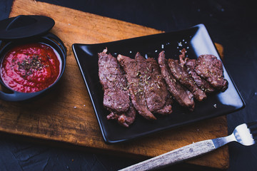 Beef steak cut into strips with tomato sauce on wood.