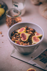 Homemade healthy granola with fresh figs and honey drizzle in a breakfast bowl on pink table.
