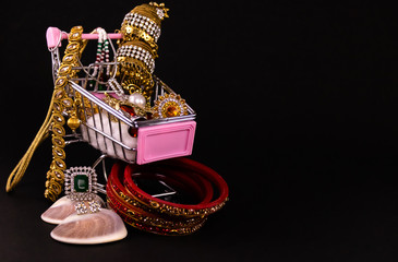 Jewellery shopping concept. Mini shopping cart full of beautiful and traditional jewellery on black background © winistudios