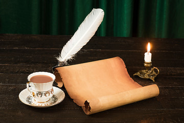 A cup of drink, a scroll of papyrus, a feather, and a candle in a candlestick against the background of green curtains