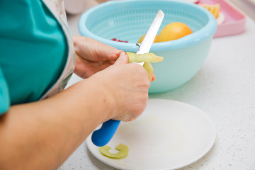 Directly above shot of Woman peeling an apple . The woman knocks on top of the apple . Female hands peeling skin off of green apple using a paring knife with bamboo plate wooden table in background .