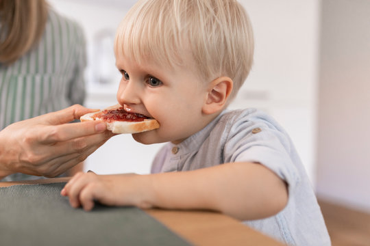 Mother feeding her cute toddler son with toast for breakfast.