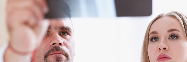 Mature male doctor hold in arm and look at xray photography discussing it with female patient portrait. Bone disease exam medic assistance cancer test healthy lifestyle hospital practice concept