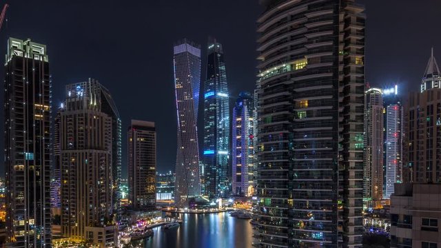 Aerial panoramic view of Dubai Marina residential and office skyscrapers with waterfront during all night timelapse with flashing lights switching off. Floating boats and yachts