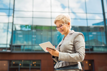 stylish adult woman in age in a suit and glasses against the background of a glass building with a...