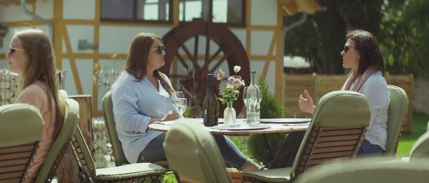 Two women sitting outside in daylight on a patio at a restaurant having a good conversation - zwei Frauen sitzen drau&szlig;en auf der Terasse in einem Restaurant in der Sonne und unterhalten sich
