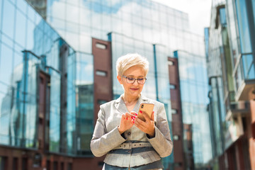 stylish adult woman in age in a suit and glasses against the background of a glass building