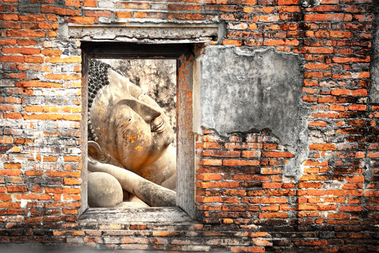 Head of reclining Buddha image behind the ancient grunge brick wall, selective focus on the face of the Buddha