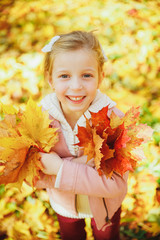 Autumn portrait of cute curly girl.Little funny girl playing with yellow leaves in the forest. Child on a walk in the autumn park. Golden autumn. toddler girl , portrait with bouquet of autumn leaves