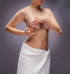 Woman examining breast on gray background