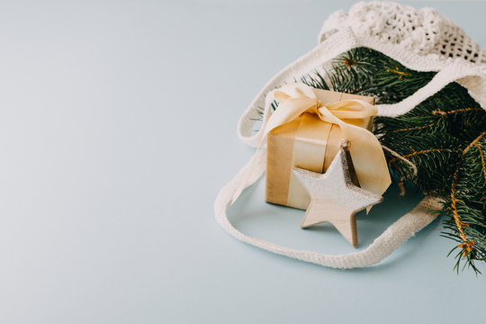 Christmas composition. New Year or Christmas flat lay, top view with trend eco friendly modern cotton net bag with fir branches, gift box and rustic style wooden star on blue background