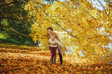 mother playing with her daughter in autumn park. Mom and her child playing together on autumn walk outdoors. Happy loving family having fun.Fashion family concept - stylish mother and child wear.