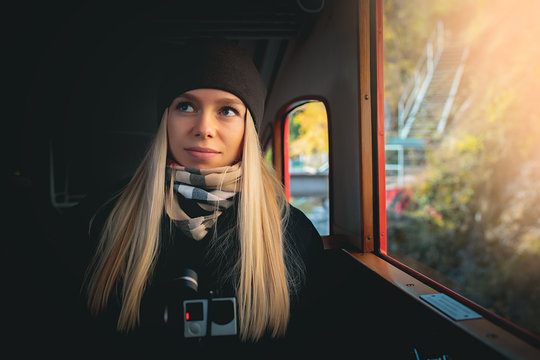 Young beautiful pretty blonde tourist girl in warm hat and coat with action camera walking at cold autumn in Europe city enjoying her travel in Zurich Switzerland in train near window