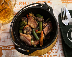 Serving the main course.  Cast iron with baked vegetables and fresh meat.  Cutlery fork and knife. Beer in a big mug. 