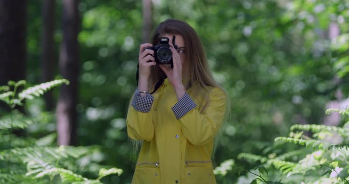 4K Portrait. Young Smiling Woman with Camera in a Rain Forest. Girl in Yellow Jacket in a Wood. Pretty Hiker Stood within tree foliage in a Green Park with Natural Sun Light.