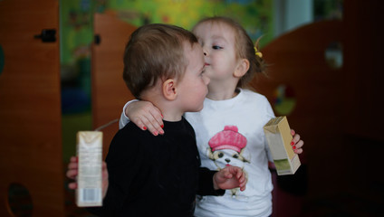Funny little boy and girl drinking juice together in kindergarten