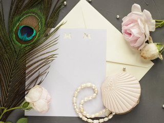 Writing letters concept. Vintage composition of pink roses, peacock feather, old casket with river pearls, postal envelope and paper. Horizontal flat lay on the dark grey background. Place for text.