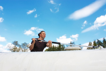 Middle aged man with brown long hairs washing a white caravan. Isolated on blue cloudy sky. Travel concept.