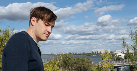 A portrait of a handsome man with beard against the background of green trees in the park.