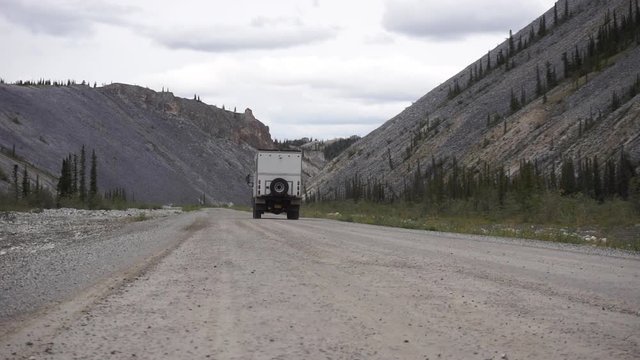 Low shot of an extreme truck camper appearing from the right of the shot on a dirt road. Dempster Highway, Canada.