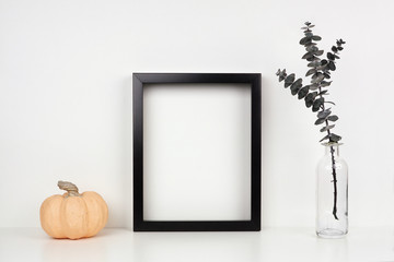 Mock up black frame with pumpkin decor and eucalyptus branch on a shelf or desk. Autumn concept....