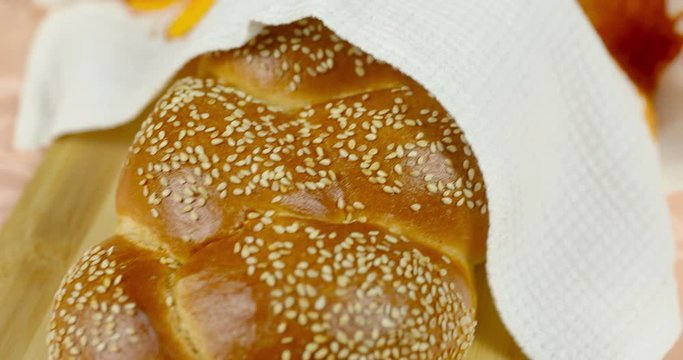 The camera moves smoothly to the Shabbat challah lying on a cutting board on a tablecloth covered with a white towel