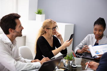 Businesswoman Using Smart Phone Sitting With Her Colleagues